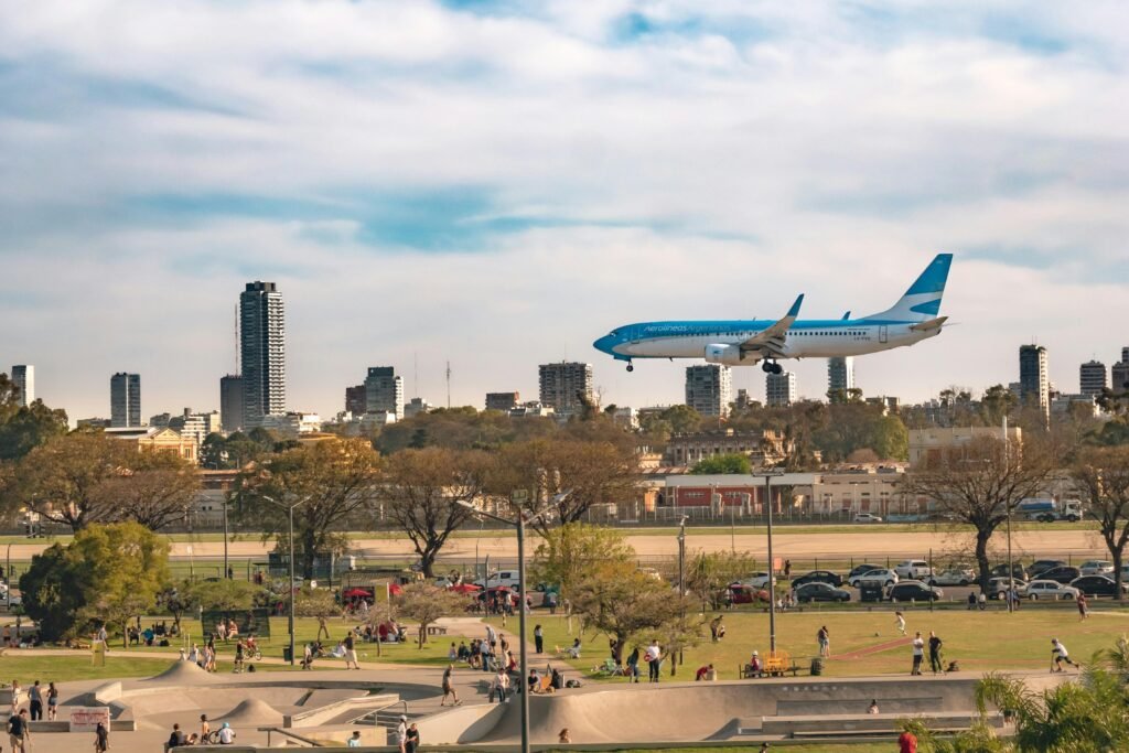 A commercial airplane flies over Buenos Aires' urban park with a city skyline backdrop.