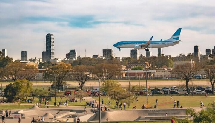 A commercial airplane flies over Buenos Aires' urban park with a city skyline backdrop.