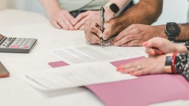 Team collaboration on paperwork with calculator and documents on a white table.