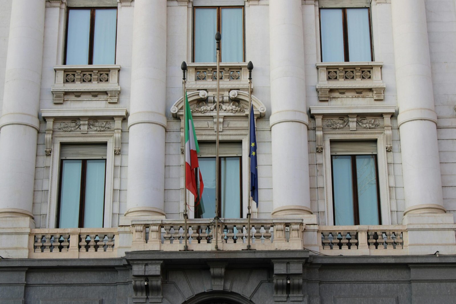 Elegant building facade with Italian and European Union flags in Milan, Italy.